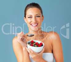 Healthiness and happiness go hand in hand. Studio shot of an attractive young woman eating a bowl of muesli and fruit against a blue background.