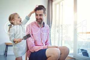Future hairstylist in the making. Shot of an adorable little girl brushing her fathers hair at home.