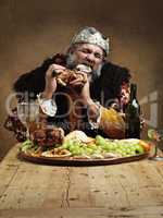 Ruling is hungry business. A mature king feasting alone in a banquet hall.