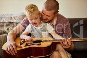 Time for another guitar lesson with Dad. Cropped shot of a father and his little son playing the guitar together at home.