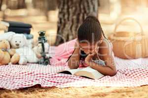 Reading opens new worlds for kids. Shot of a little girl reading a book with her toys in the woods.