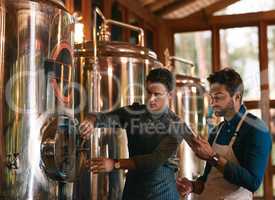 Lets hope this batch is a good one. Shot of two young working men doing inspection of their beer making machinery inside of a beer brewery during the day.