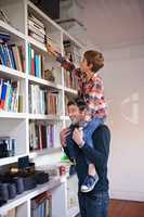 I want that one at the top. A young boy sitting on his dads shoulders to reach a book in their book shelf.