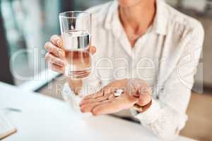 Vitamins are vital for our immune systems. Closeup shot of an unrecognisable businesswoman holding a glass of water and medication in an office.