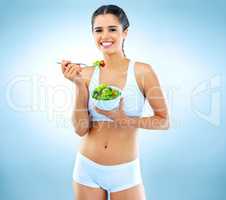 Dont eat less, eat right. Studio portrait of an attractive young woman eating a salad against a blue background.