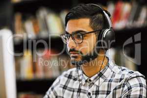 This all going to pay off soon. Closeup shot of a focused young man sitting and working on a computer in a library while listening to music.