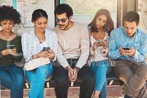 Looks like Im the only one not busy on my phone =. Shot of a group of focused young friends seated next to each other while texting and browsing on their cellphones outside during the day.