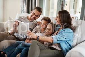 The best way to incorporate learning into playtime. Shot of a happy young family of four using a digital tablet together on the sofa at home.