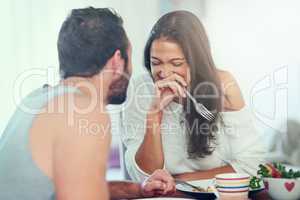 He loves making her laugh. Shot of a young man telling his girlfriend a joke while they enjoy breakfast at home.