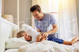 Wake up sleepy head. Shot of a cheerful young man trying to wake up his son from sleeping on a bed at home in the morning.