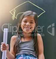 Someday I will achieve all my dreams. Portrait of a little girl posing against a blackboard with a drawing of a graduation cap.