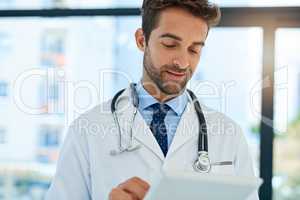 Getting a second opinion online. Shot of a busy doctor checking a patients medical records on his tablet.