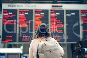 Let the journey begin. Rearview shot of an unrecognizable young woman looking at an arrivals and departures board while standing in an airport.