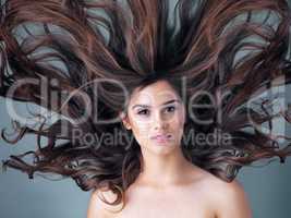 Big hair, big dreams. Studio shot of a beautiful young woman posing against a gray background.