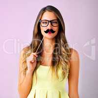 Dont take life too serious. Studio shot of a young woman holding a mustache prop to her face against a pink background.