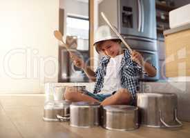 Hes a born percussionist. Shot of a happy little boy playing drums with pots on the kitchen floor while wearing a bowl on his head.