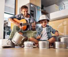 Its a father-son collaboration. Shot of a happy father accompanying his young son on the guitar while he drums on a set of cooking pots.
