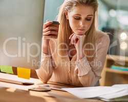 Working thorough her coffee break. Shot of a young businesswoman sitting at her desk in an office reading paperwork.