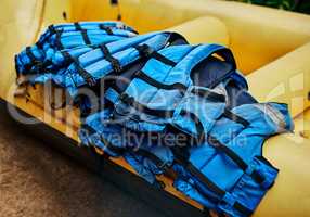 These guys can save your life. Shot of a pile of river rafting life jackets lying on top of a rubber river rafting boat outside during the day.