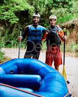 Weve been doing this since we were kids. Portrait of two cheerful young men wearing protective gear while each holding a paddle to go river rafting.