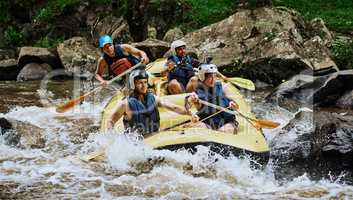 Keep her steady guys. Shot of a group of determined young men on a rubber boat busy paddling on strong river rapids outside during the day.