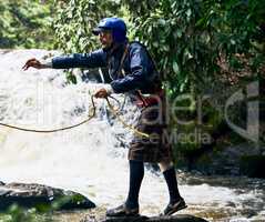 Hold on to the rope. Shot of a focused middle aged man wearing protective gear while throwing out a rope to somebody in a river outside during the day.