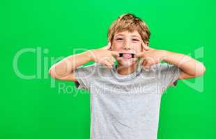 Hes a cheeky little one. Studio portrait of a young boy making a funny face against a green background.