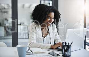 Quickly sending out the good news to the team. Shot of a young businesswoman working and in good spirits at her office desk.
