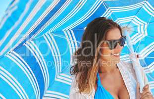Beat the heat. Shot of a beautiful young woman holding a beach umbrella on a summers day.