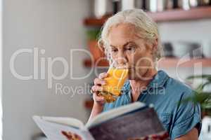 Its not a diet, its a way of life. Shot of a mature woman reading a book while having orange juice at home.