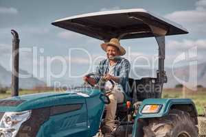 Off to the fields we go. Shot of a mature man driving a tractor on a farm.