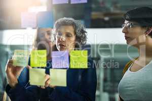 Making mind maps work for them. Shot of a group of colleagues working with adhesive notes on a glass wall in the office.