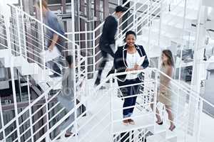 Busy making success happen. Portrait of a young professional standing on a stairs with colleagues rushing around her.