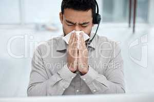 Got the sniffles. Shot of a young businessman blowing his nose while working in a call centre.