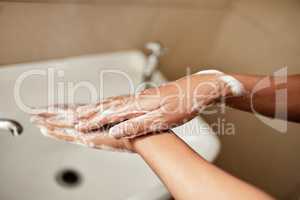 Whatever you do, wash your hands. Cropped shot of a woman washing her hands with soap in the bathroom sink at home.