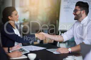 Sealing their partnership with a handshake. Shot of two smiling businesspeople shaking hands together in a boardroom.