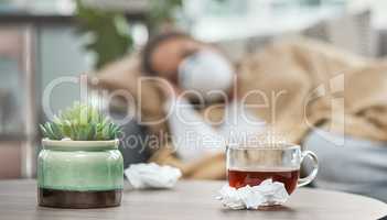 On the road to recovery. Shot of dirty tissues and a cup of tea on a table next to a woman lying sick at home.