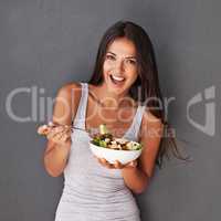Bite into this. Portrait of a healthy young woman eating a salad against a gray background.