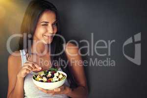 You're gonna love this. Portrait of a healthy young woman eating a salad against a gray background.