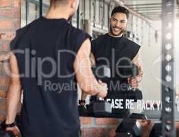 Workout to impress yourself. Shot of a sporty young man looking at himself in a mirror while exercising with dumbbells in a gym.