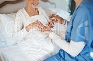 Reliable treatment is in her hands. Shot of a nurse giving a senior woman her medication to take with a glass of water in bed.