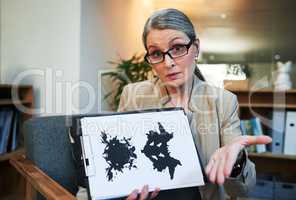 What you see says a lot. Portrait of a mature psychologist holding up an inkblot test during a therapeutic session.