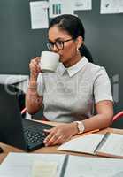 Coffee gets me through it all. Shot of a young businesswoman drinking coffee while working on a laptop in an office.