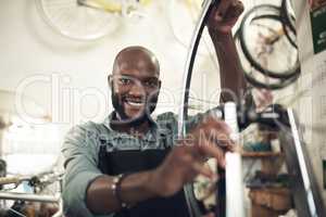 I love what I do. Shot of a handsome young man standing alone in his shop and repairing a bicycle wheel.