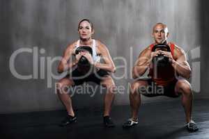 Train insane or remain the same. A man and woman working out with kettle bells at the gym.