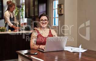 Im happy to sort out our budgets. Portrait of a cheerful young woman working on a laptop and doing paperwork while being seated at a table at home.