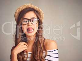 Lifes a little weird. Embrace it. Studio shot of an attractive young woman playfully touching her nose with her tongue against a gray background.