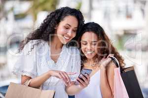 Best friends share the best deals with you. Shot of two young women using a smartphone while shopping against an urban background.
