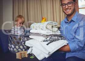 Dad does it all. Portrait of a young man holding a load clean laundry with his son in the background.