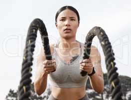 Work hard, stay consistent and be patient. Shot of an athletic young woman doing heavy rope training outside.